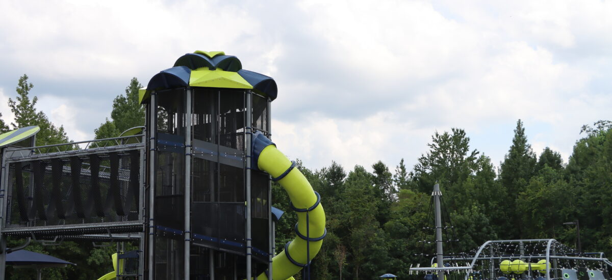 Large and small playground structures in a green field.