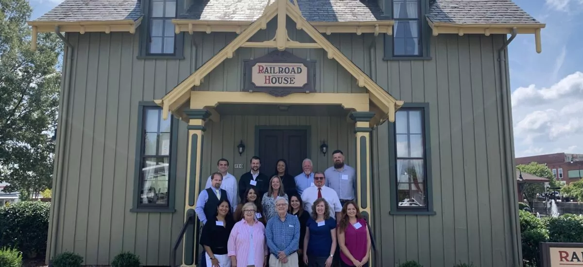 Leadership Sanford group standing in front of Railroad House, a green building with yellow trim