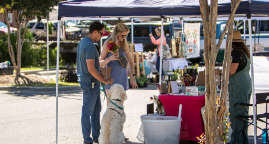 Two people shop with their dog at the sanford farmers market